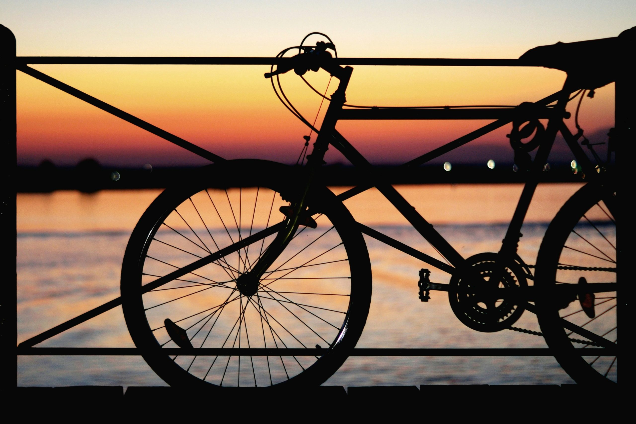 Imagen de tres cuartos de una bicicleta apoyada sobre una baranda en el atardecer, con el mar y luces de fondo. La imagen tiene como objetivo representar la portada de la columna "Un día sin auto no alcanza" en conmemoración del Día Mundial sin Automóvil.